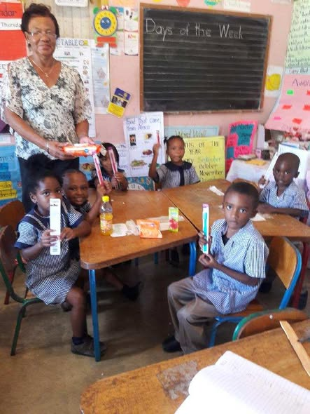 A Simunye volunteer and students in a classroom displaying donated dental hygiene supplies during a Simunye outreach trip.